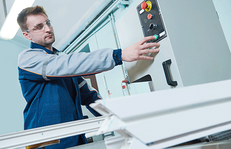 Mężczyzna w szaro niebieskim stroju ochronnym naciska zielony przycisk maszyny do produkcji wysokiej jakości profili plastikowych.